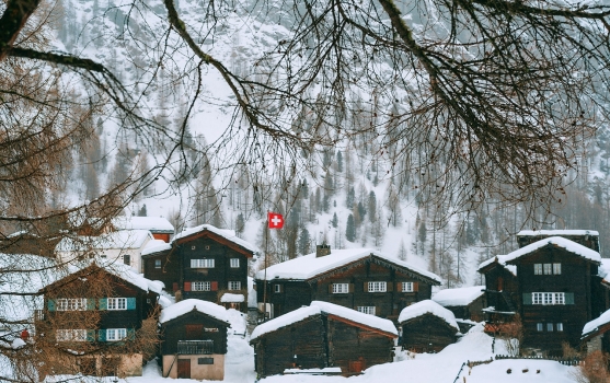 Schweizer Flagge auf dem Dach von schneebedeckten Dorfhäusern auf einem hügeligen Gelände in der Schweiz